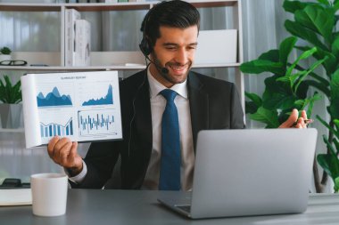 Kulaklık takan bir iş adamı online toplantı sırasında bilgisayarla finansal veri ya da BI kağıdı sunar. Etkili uzaktan çalışmanın sanal toplantı sunumuyla uzaktan çalışma konsepti. Coşkulu