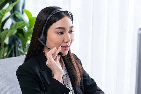 Happy asian call center operator with headset and microphone working on workstation. Smiling female operator provide customer support service. Supportive and professional call center woman. Jubilant