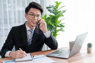 Ofis masasında akıllı telefonuyla bilgisayar başında çalışan bir iş adamı. Akıllı bir yönetici finansal iş verilerini araştırıyor ya da stratejik işler planlıyor, telefonla konuşuyor. Sevinçli.