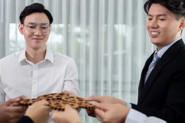 stock image Closeup hand holding wooden gear by businesspeople wearing suit for harmony synergy in office workplace concept. Group of people hand making chain of gears into collective form for unity symbol.