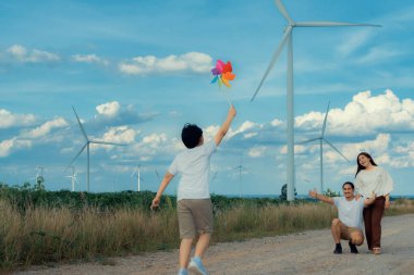 Progressive happy family enjoying their time at wind farm for green energy production concept. Wind turbine generators provide clean renewable energy for eco-friendly purposes.