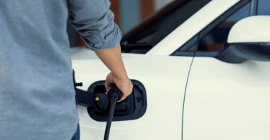 Closeup progressive asian man install cable plug to his electric car with home charging station. Concept of the use of electric vehicles in a progressive lifestyle contributes to clean environment.
