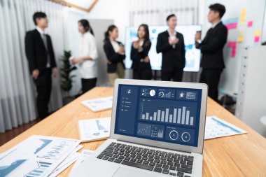 Focus laptop monitor display dashboard report by business intelligence, analyzed financial data for planning market strategy with blur background of standing office worker discussing in harmony office