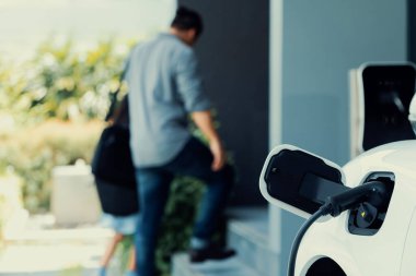 Arka planda bulanık baba ve kızının yürüdüğü şarj istasyonunda elektrikli araba şarj etmeye odaklan. Sağlıklı çevre yaşam tarzı konsepti için yenilikçi yeşil ve temiz enerji aracı.