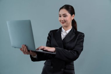 Kendine güvenen genç iş kadını izole edilmiş bir zeminde duruyor ve resmi siyah takım elbiseyle dizüstü bilgisayarda çalışıyor. Ofisteki kadın ya da yönetici, zeki ve profesyonel görünümlü. Coşkulu.
