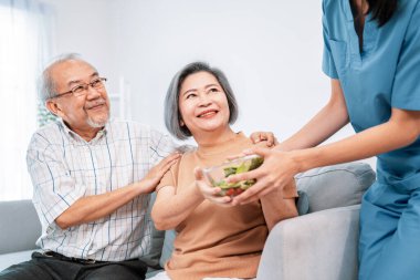 A female nurse serves a bowl of salad to a contented senior couple. Health care and medical assistance for the elderly, nursing home for pensioners.