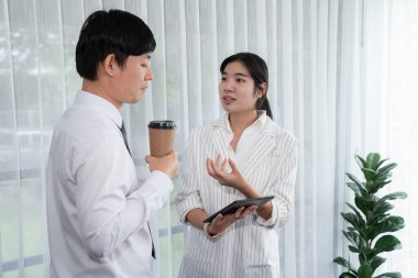 Manager advising guiding younger colleague with tablet in workplace. Couple businesspeople in formal wear working together on financial strategy as concept of teamwork and harmony in office.