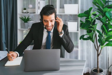 Erkek çağrı merkezi operatörü ya da telesales temsilcisi ofis masasında otururken kulaklık takıyor ve müşteri desteği sağlayan ya da ikna edici satış yapan müşteriyle sohbet ediyor. coşkulu