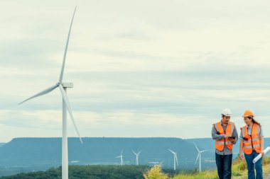 Erkek ve kadın mühendisler kırsal kesimdeki bir tepenin tepesinde ya da dağda rüzgar çiftliğinde çalışıyorlar. Yenilenebilir ve sürdürülebilir enerjinin gelecekteki üretimi için yenilikçi idealler.