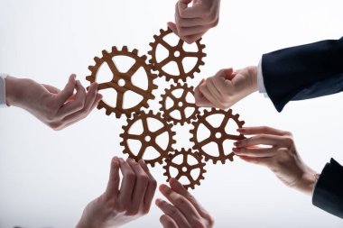 Hand holding wooden gear by businesspeople wearing suit for harmony synergy in office workplace concept. Isolated background. Bottom view of people hand make chain of gear into collective unity symbol