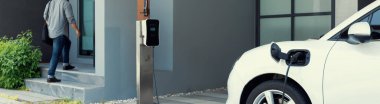 Progressive asian man and electric car with home charging station. Concept of the use of electric vehicles in a progressive lifestyle contributes to a clean and healthy environment.