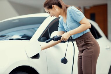 Progressive woman install cable plug to her electric car with home charging station. Concept of the use of electric vehicles in a progressive lifestyle contributes to clean environment.
