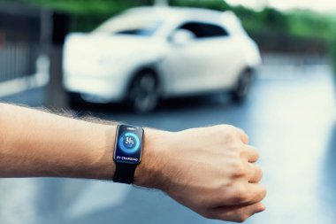 Yakın çekim odaklı giyilebilir saat şehirdeki şarj istasyonunda şarj edilen elektrikli araba aküsünün durumunu gösteriyor. Dijital arayüz, akıllı kayıtta EV araba görüntüsü verisi.