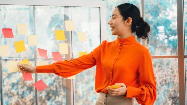 İş adamları ofisteki proje planlama kurulunda çalışıyor ve proje gelişimini analiz etmek için iş arkadaşlarıyla sohbet ediyorlar. Düzenli olması için cama yapıştırılmış yapışkan notlar kullanıyorlar. Jivy