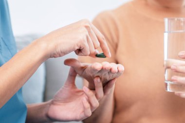 Contented senior woman taking medicines while her caregiver advising her medication. Medication for seniors, nursing house, healthcare at home.