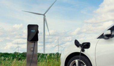 Progressive combination of wind turbine and EV car, future energy infrastructure. Electric vehicle being charged at charging station powered by renewable energy from wind turbine in the countryside.