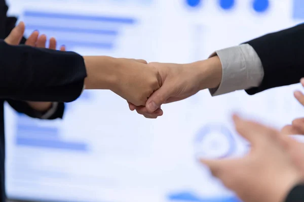 Closeup office worker shake hand business team leader manager for strong teamwork in office to promote harmony concept after successful agreement or meeting with dashboard report on screen background.