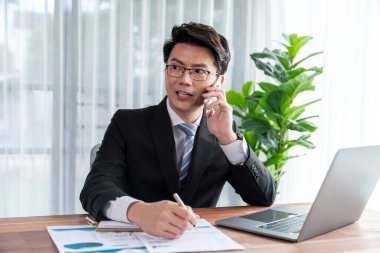 Ofis masasında akıllı telefonuyla bilgisayar başında çalışan bir iş adamı. Akıllı bir yönetici finansal iş verilerini araştırıyor ya da stratejik işler planlıyor, telefonla konuşuyor. Sevinçli.