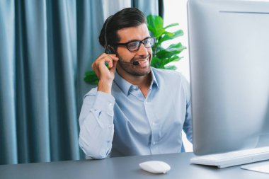 Erkek çağrı merkezi operatörü ya da telesales temsilcisi ofis masasında oturmuş kulaklık takıyor ve müşteri hizmetleri desteği sağlayan ya da satış yapan müşteriyle sohbet ediyor. coşkulu