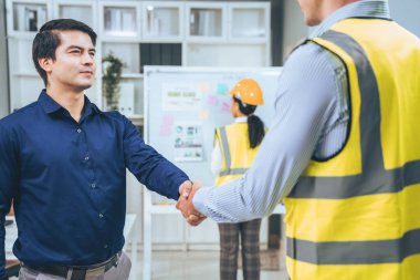An engineer with a protective vest handshake with an investor in his office. Following a successful meeting, employee and employer form a partnership.