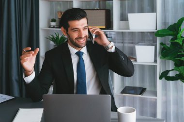 Çalışkan işadamı, ofisindeki dizüstü bilgisayarla cep telefonlu, modern, çalışkan ofis çalışanı yaşam biçimi konsepti olarak çalışırken müşterileriyle telefonda konuşmakla meşgul. Coşkulu