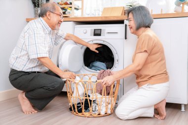 Senior couple working together to complete their household chores at the washing machine in a happy and contented manner. Husband and wife doing the usual tasks in the house.