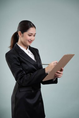 Kendine güvenen genç iş kadını, izole edilmiş bir zeminde elinde bir pano ve resmi siyah takım elbiseyle poz veriyor. Ofisteki kadın ya da yönetici, zeki ve profesyonel görünümlü. Coşkulu.