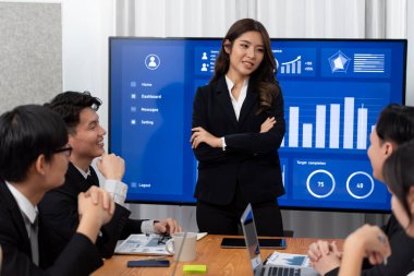 Confidence and young asian businesswoman give presentation on financial business strategy in dashboard report display on screen to colleagues in conference room meeting as harmony in workplace concept