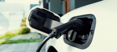 Closeup electric vehicle plugged-in with cable from charging point powered for progressive concept by alternative clean energy rechargeable EV car at home charging station.