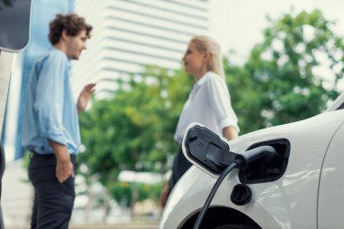 Kamu şarj istasyonuna bağlı park-elektrikli araba bulanık ilerici iş adamları kahve, konut apartmanı ve çevre dostu konsept için konut geçmişi tutuyor..