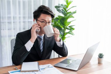 Ofis masasında akıllı telefonuyla bilgisayar başında çalışan bir iş adamı. Akıllı bir yönetici finansal iş verilerini araştırıyor ya da stratejik işler planlıyor, telefonla konuşuyor. Sevinçli.