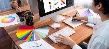 Grafik tasarımcısı, modern dijital stüdyo işyerinde profesyonel grafik ekibiyle benzersiz bir tasarım yaparken bilgisayar dizüstü bilgisayar ve grafik çizim kalemi üzerinde çalışır. Panorama çekimi. İnceleyin