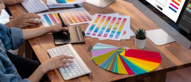 Grafik tasarımcısı, modern dijital stüdyo işyerinde profesyonel grafik ekibiyle benzersiz bir tasarım yaparken bilgisayar dizüstü bilgisayar ve grafik çizim kalemi üzerinde çalışır. Panorama çekimi. İnceleyin