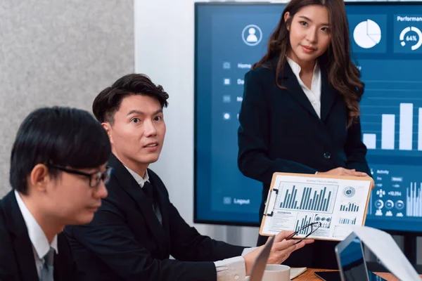 Confidence and young asian businesswoman give presentation on financial business strategy in dashboard report display on screen to colleagues in conference room meeting as harmony in workplace concept