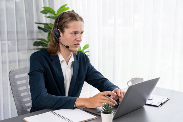 Male customer service operator or telesales agent sitting at desk in office, wearing headset and engage in conversation with client to provide support or close sales. Call center portrait. Entity