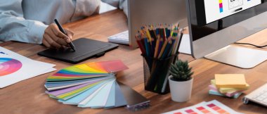 Grafik tasarımcısı, modern dijital stüdyo işyerinde profesyonel grafik ekibiyle benzersiz bir tasarım yaparken bilgisayar dizüstü bilgisayar ve grafik çizim kalemi üzerinde çalışır. Panorama çekimi. İnceleyin