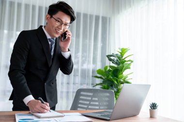 Ofis masasında akıllı telefonuyla bilgisayar başında çalışan bir iş adamı. Akıllı bir yönetici finansal iş verilerini araştırıyor ya da stratejik işler planlıyor, telefonla konuşuyor. Sevinçli.