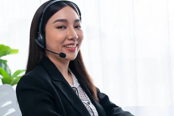 Happy asian call center operator with headset and microphone working on workstation. Smiling female operator provide customer support service. Supportive and professional call center woman. Jubilant