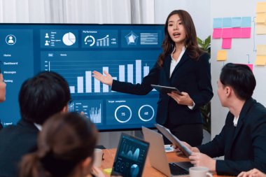 Confidence and young asian businesswoman give presentation on financial business strategy in dashboard report display on screen to colleagues in conference room meeting as harmony in workplace concept