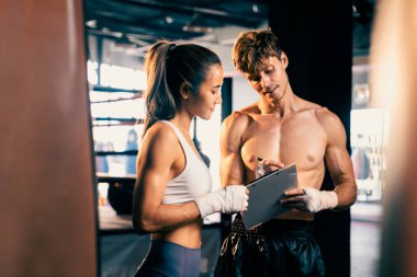 Asyalı bayan Muay Thai boksörü ve kişisel boks antrenörü spor salonundaki fiziksel ilerlemesini tartışıyor. Vücut kası gelişimine ve boks performansına bağlılığını yansıtıyor. Impetus