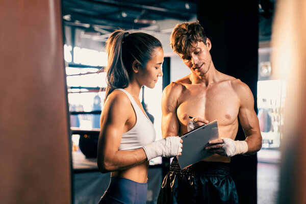 Asian female Muay Thai boxer and her personal boxing trainer discussing on her physical progress in the gym reflecting commitment to her body muscle growth and boxing performance. Impetus
