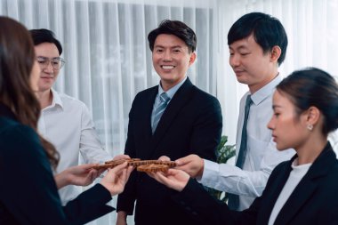 Closeup hand holding wooden gear by businesspeople wearing suit for harmony synergy in office workplace concept. Group of people hand making chain of gears into collective form for unity symbol.