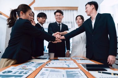 Closeup business team of suit-clad businessmen and women join hand stack together and form circle. Colleague collaborate and work together to promote harmony and teamwork concept in office workplace.