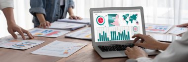 Panorama shot analyst team utilizing BI Fintech to analyze financial report with laptop. Businesspeople analyzing BI power dashboard displayed on laptop screen for business insight. Scrutinize clipart