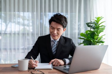 Ofis masasında dizüstü bilgisayarda çalışan bir iş adamı. Akıllı yönetici finansal iş verilerini araştırıyor ya da masada bilgisayarla stratejik iş pazarlaması planlıyor. Sevinçli.