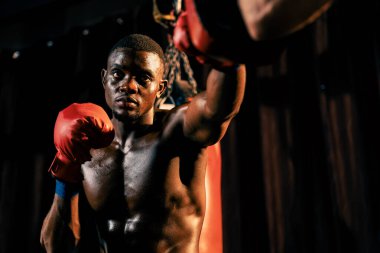 Afrika kökenli siyah boksör antrenöre yumruk atıyor ya da spor salonunda boks çantası olarak boks eldiveni takıyor. Profesyonel boks maçı için güç ve dayanıklılık eğitimi. Impetus