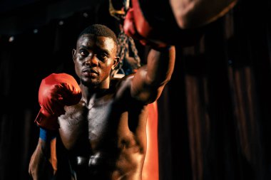 Afrika kökenli siyah boksör antrenöre yumruk atıyor ya da spor salonunda boks çantası olarak boks eldiveni takıyor. Profesyonel boks maçı için güç ve dayanıklılık eğitimi. Impetus