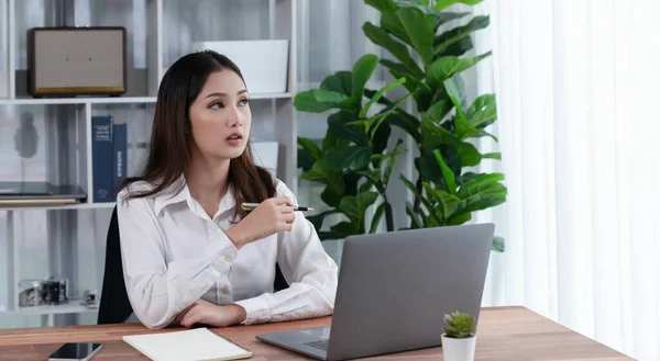 stock image Young asian enthusiastic businesswoman at modern office desk using laptop to work and write notes. Diligent and attractive office lady working on computer notebook in her office work space.