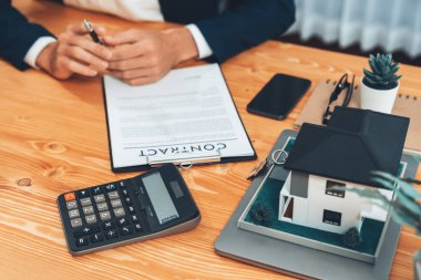 Emlakçı vergi ve faizi hesaplıyor, müşteriyle emlak satın alma ve ev kredisi başvurusunda bulunma şartları. Finansal danışman, yatırım bütçesini hesap makinesiyle yönetiyor. Varlık