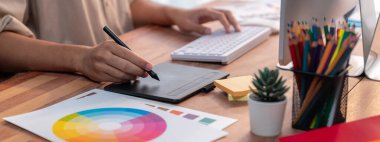 Grafik tasarımcısı, modern dijital stüdyo işyerinde profesyonel grafik ekibiyle benzersiz bir tasarım yaparken bilgisayar dizüstü bilgisayar ve grafik çizim kalemi üzerinde çalışır. Panorama çekimi. İnceleyin
